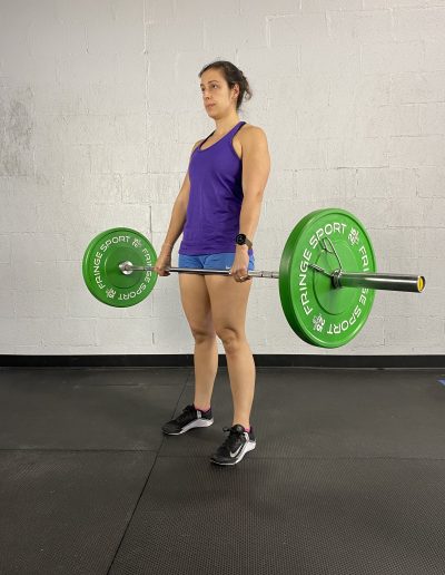 woman standing at the top of a deadlift with a barbell and weight